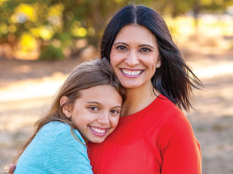 Woman being hugged by young girl in outdoor setting both are smiling